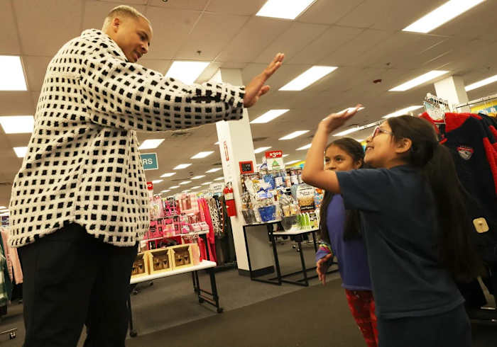 Customers Jhoanna Castro, 10, center, and Evelyn Chimbay, 7, get a high-five from New England Patriots tight end Pharaoh Brown at a surprise holiday payoff event at Brockton Citi Trends on Tuesday, Dec. 12, 2023.